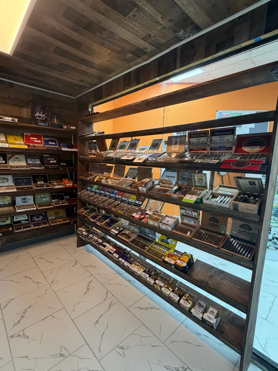 Wood-lined walk-in humidor with tilted shelves of boxed and loose premium cigars