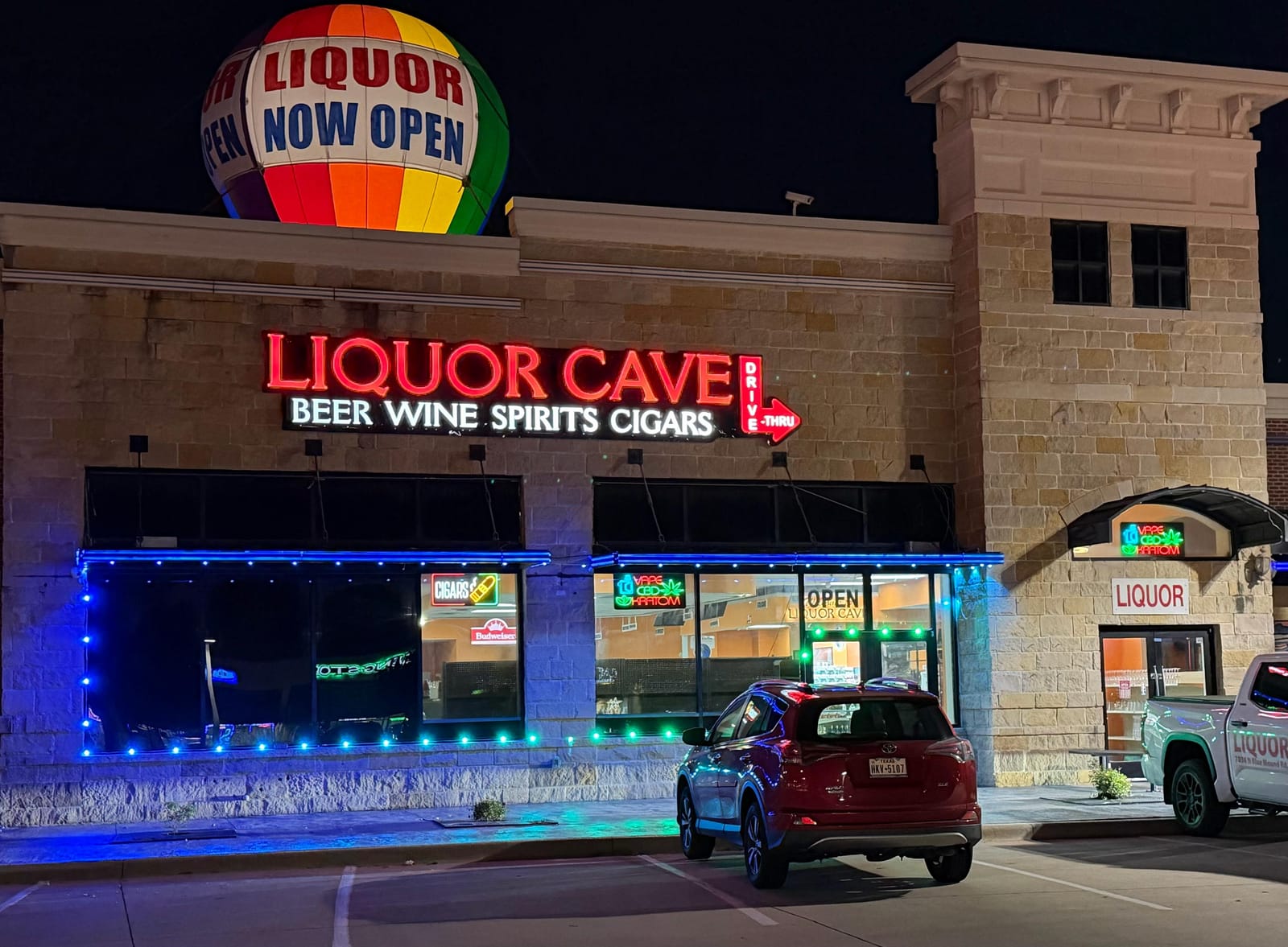 Liquor Cave storefront at night: the red neon sign reads Liquor Cave, beer, wine, spirits, cigars, with a drive-thru lane on the right