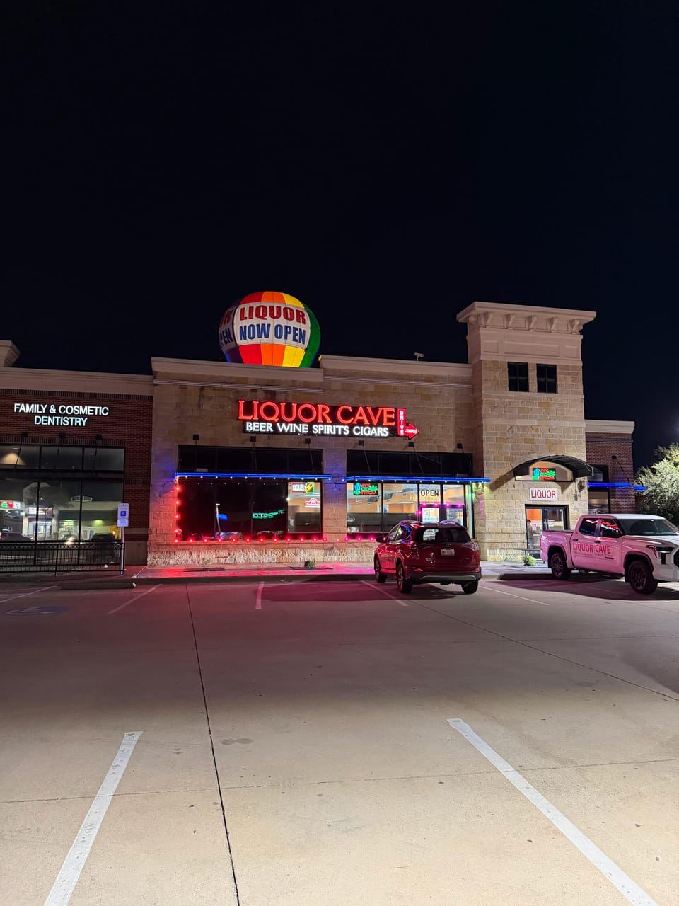 The Liquor Cave building at night with a Liquor Now Open balloon floating above the neon sign